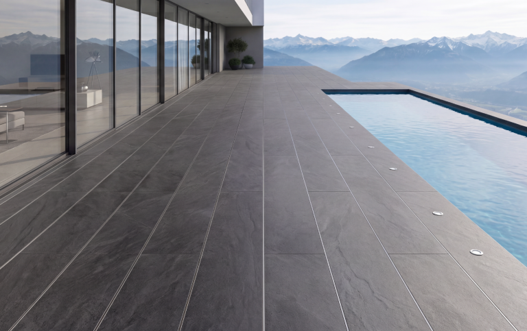 Professionelle Bodenlösung für Garten und Outdoor Living Terrasse mit dunklem Bodenbelag und Infinity-Pool, Berglandschaft im Hintergrund.
